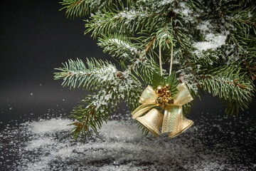 Christmas decoration with bells, a branch of a Christmas tree and artificial snow on a black background.