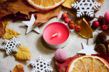 November composition. Candle on linen fabric with autumn leaves, decorative snowflakes, dried oranges and different decor. Selective Focus, top view, flat lay. Hugge concept with copy space.