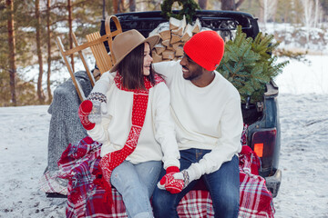 Obraz premium Happy multiracial couple in white sweatshirts during a trip to the forest for the christmas tree.