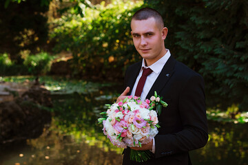 Young groom poses for the first time on camera. Wedding photosession of guy in park.