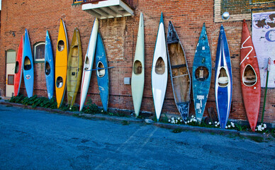Colorful, old kayaks leaning against a brick wall