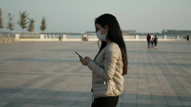 brunette Girl in mask in outdoor look to the mobile phone and wear the mask