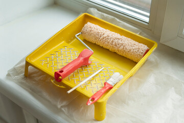 Fototapeta na wymiar Yellow painting tray cuvette and paint roller with red handle, made of synthetic fiber.