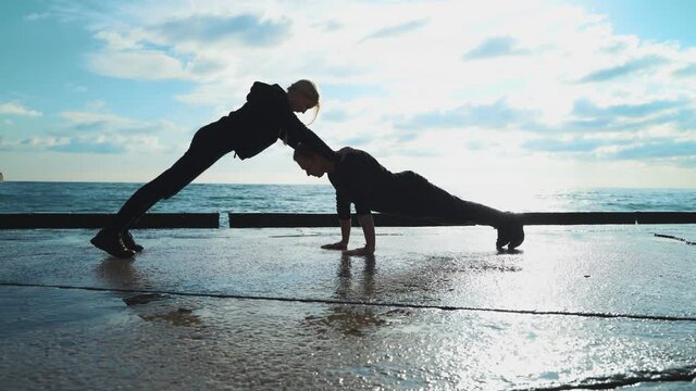 Young couple in sportswear are engaged in morning exercises against the background of the sea. The guy and the girl go in for sports together. 4k