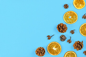 Seasonal autumn flat lay with dried orange slices and fir cones in corner of blue background with empty copy space