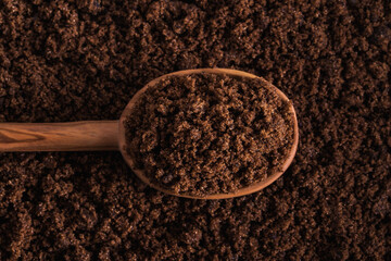 Dark muscovado sugar, known as Barbados sugar on wooden spoon and textured sugar background.