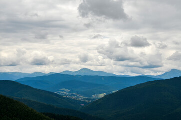 Naklejka premium Landscape with forest, mountains and small Carpathian village in the valley under cloudy sky 