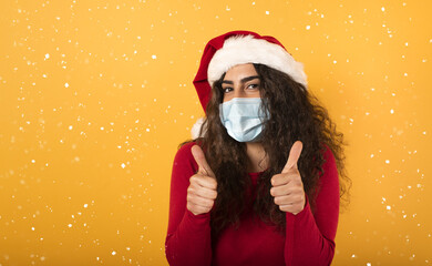 Woman with Christmas hat is optimistic about the defeat of covid 19 coronavirus. yellow background.