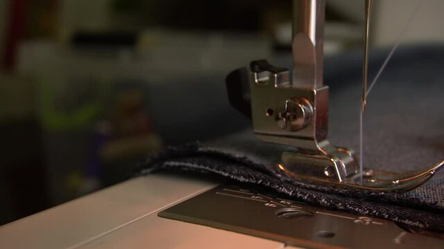The seamstress sews denim on a sewing machine, advances the fabric with his fingers. The movement of the foot and needle when sewing denim on the sewing machine.