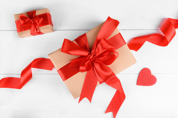 Gift box wrapped in craft recycled paper with red ribbon bow and red heart on a white wooden backgroud. Christmas or San Valentino present, top view
