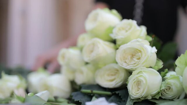 Flowers of white roses lie in a pile on the table against the background of a florist girl. Preparing flowers for decoration.