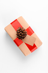 Christmas gift tag mock up with gift box wrapped in craft recycled paper with red ribbon and pine cones on a white backgroud. Christmas or San Valentino present, top view, copy space