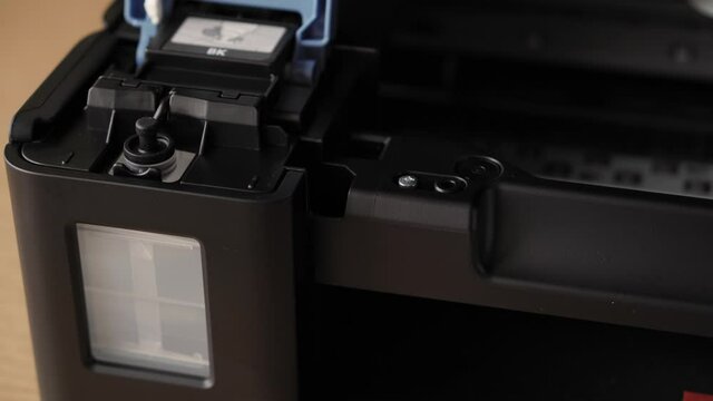 Video instruction, technology, media, office, stationery concept - close-up of male hands preparing new inkjet printer for launch. step 8: pouring ink - open blue tank cover grab and remove black cap