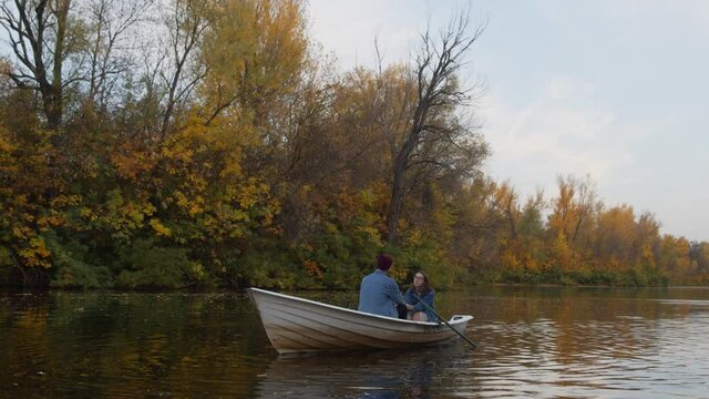 A handsome guy and a beautiful girl sits in a boat on a lake in a fairy autumn forest