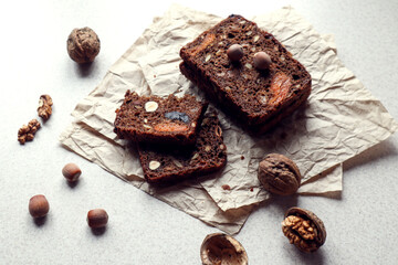 Pieces of baked bread with nuts, prunes and dried apricots on packaging paper, forest nuts and walnuts next to each other, side view, close - up-the concept of using nuts in bakery products