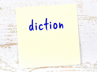 Yellow sticky note on wooden wall with handwritten word diction