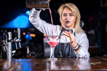Portrait of girl barman places the finishing touches on a drink at bar