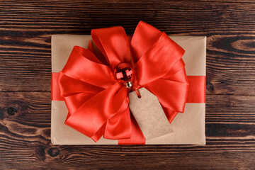 Gift box wrapped in recycled kraft paper with red ribbon bow and Christmas ball on a wooden background. Gift for Christmas or San Valentino, top view