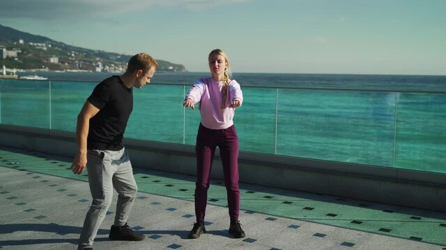 A young guy makes a girl go in for sports, runs around her and yells at her. The guy aggressively teaches the girl to do the exercises correctly. 4k