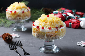 Festive salad with chicken, pineapple, cheese and eggs in portioned bowls on dark gray background. New Year still life. Horizontal format