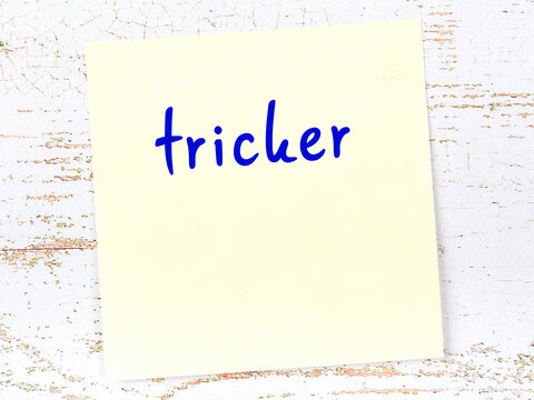 Yellow sticky note on wooden wall with handwritten word tricker