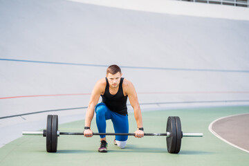 Young guy raises the bar in the stadium, outdoor workout