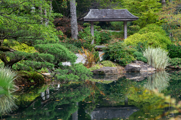 A pagoda in Japanese garden surrounded by a variety of plants, trees and water.