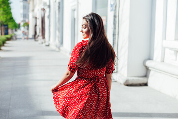 Beautiful fashionable brunette woman in summer red dress on the street of the city