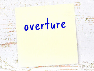 Yellow sticky note on wooden wall with handwritten word overture