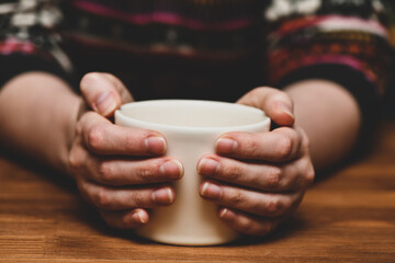 Young woman holding hot cocoa or coffee cup. Autumn or winter moody weekend, New Year, and Christmas background. Lazy day, light breakfast, quarantine, stay home, cozy scene, hygge concept.