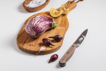 Closeup of nubia eggplant, garlic, and shallots on a small wooden cutting board - obrazy, fototapety, plakaty