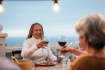 Senior multiracial people cheering with red wine at dinner outdoor on patio