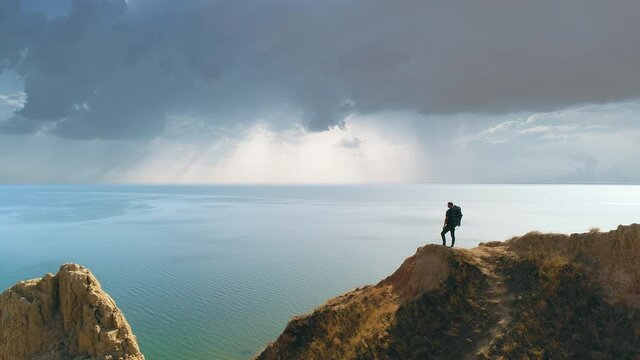 The tourist is standing on the mountain cliff on the seascape background