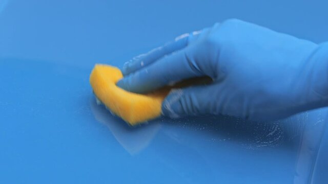 A woman in blue rubber gloves cleans the table with a sponge with a foaming detergent. Soap foam on a glass surface close-up, cleaning the bathroom sink, disinfection, surface cleaning 