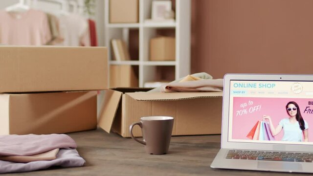 PAN of cardboard boxes and laptop with web page of online store open on it are on table in office of small retail company