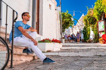 Young man sitting by the trulli houses in Alberobello, province Bari, region Puglia, Italy....