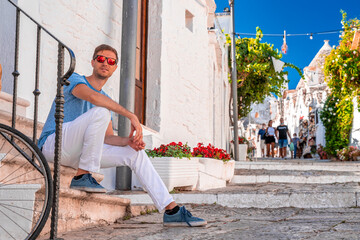 Young man sitting by the trulli houses in Alberobello, province Bari, region Puglia, Italy....