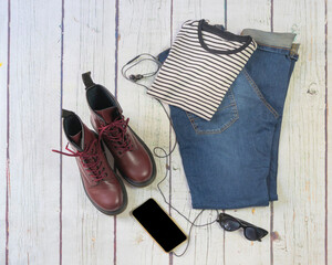 Still life with burgundy military boots, jeans, smartphone and headphones