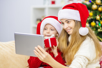 A young mother with her daughter is calling relatives online using a tablet computer for congratulations on the holidays