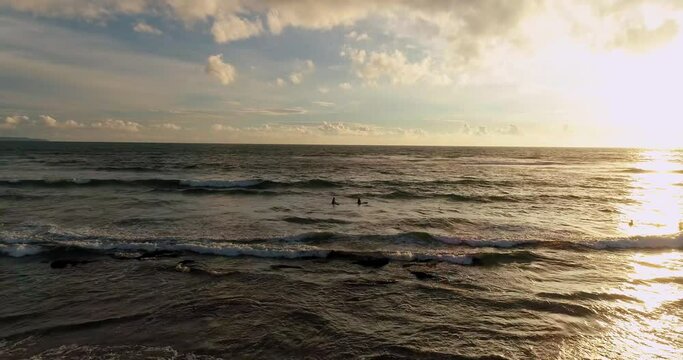 Drone shot beach coastline of Bali island at sunset. Surfers catching waves.