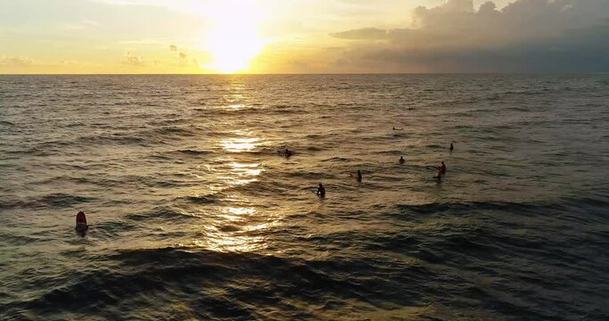 Drone video of surfers waiting in the ocean for perfect wave at sunset.