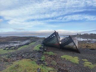 Shipwreck on a beach of pebbles under a bright blue cloudy sky Island of Mull Scotland