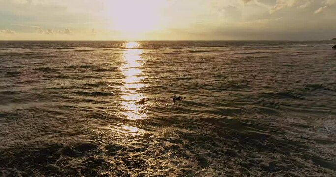 Aerial view of surfers catching waves at sunset ocean.