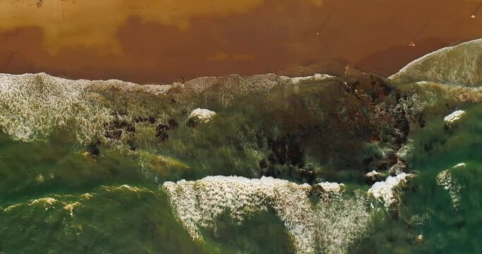 Top down drone video of waves breaking on empty rocky beach.