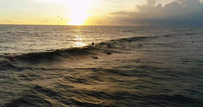 Drone video of surfers catching the waves at sunset.