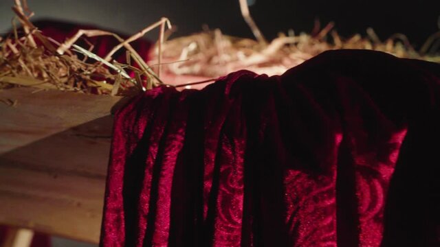 Close up slider shot of a Christmas Jesus manger. The crip contains straw which is shining mystical and a red scarf is artful laying on the corner.