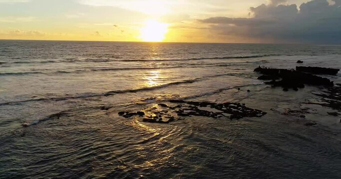 Drone view of ocean and rocky coastline at sunset.