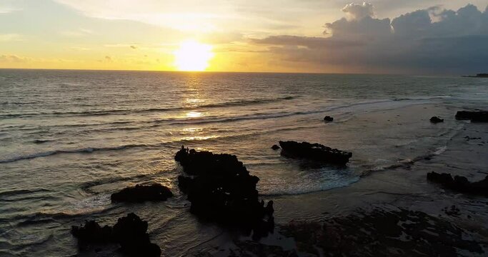 Drone shot of the ocean at sunset and people walking on the sandy beach