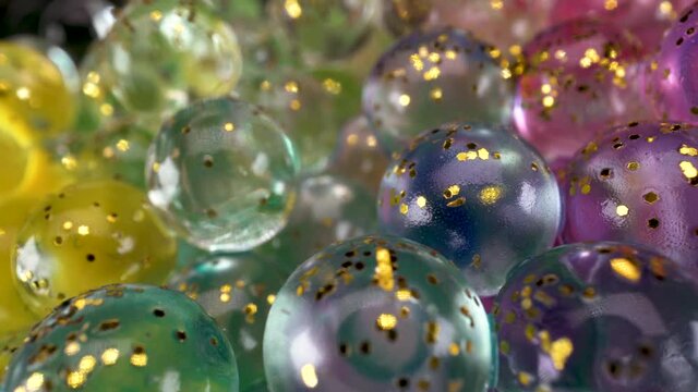 Macro view of glass spheres wet abstract light reflections with colors and golden glitter, interesting 4k bright fun background footage