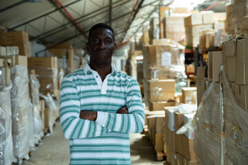 Portrait of successful African American warehouse manager standing with arms crossed against boxes of goods